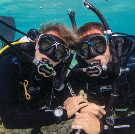 Two scuba divers holding hands under water and posing for the camera